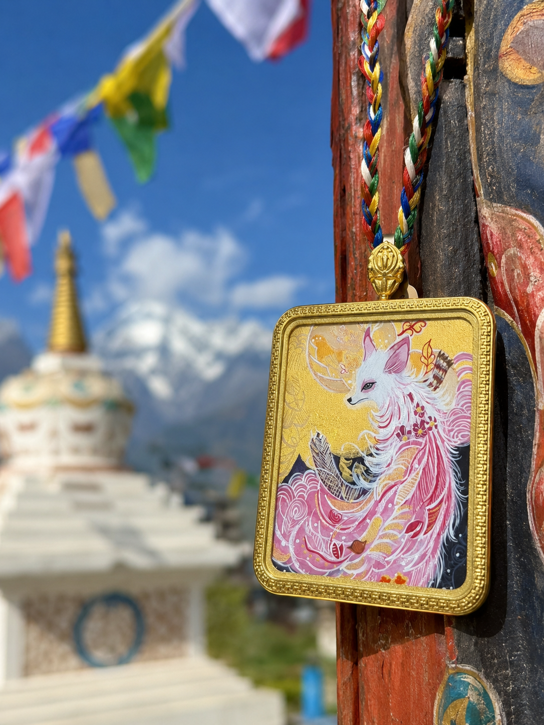 Nine-Tailed Fox pendant hanging beside a painted post, with prayer flags behind