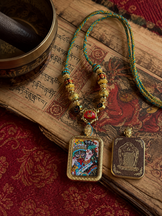 Zaki Lhamo pendant and braided necklace laid over illustrated pages and red patterned fabric
