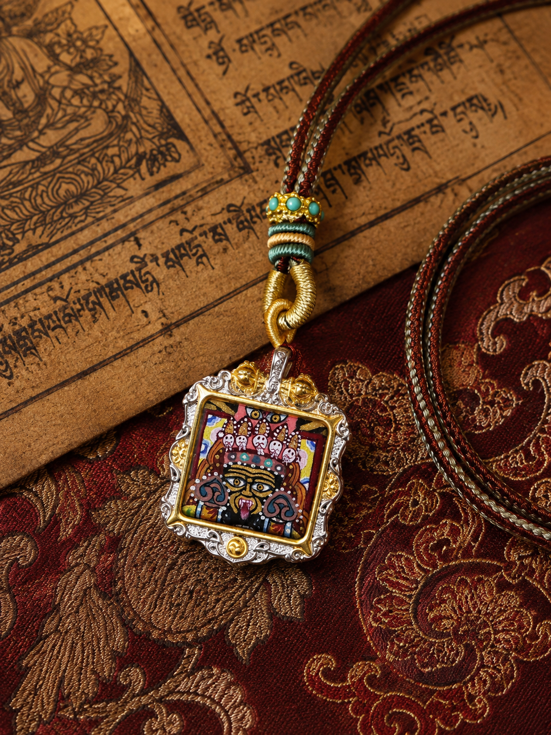 Square Zaki Lhamo ghau pendant laid on patterned fabric beside printed pages