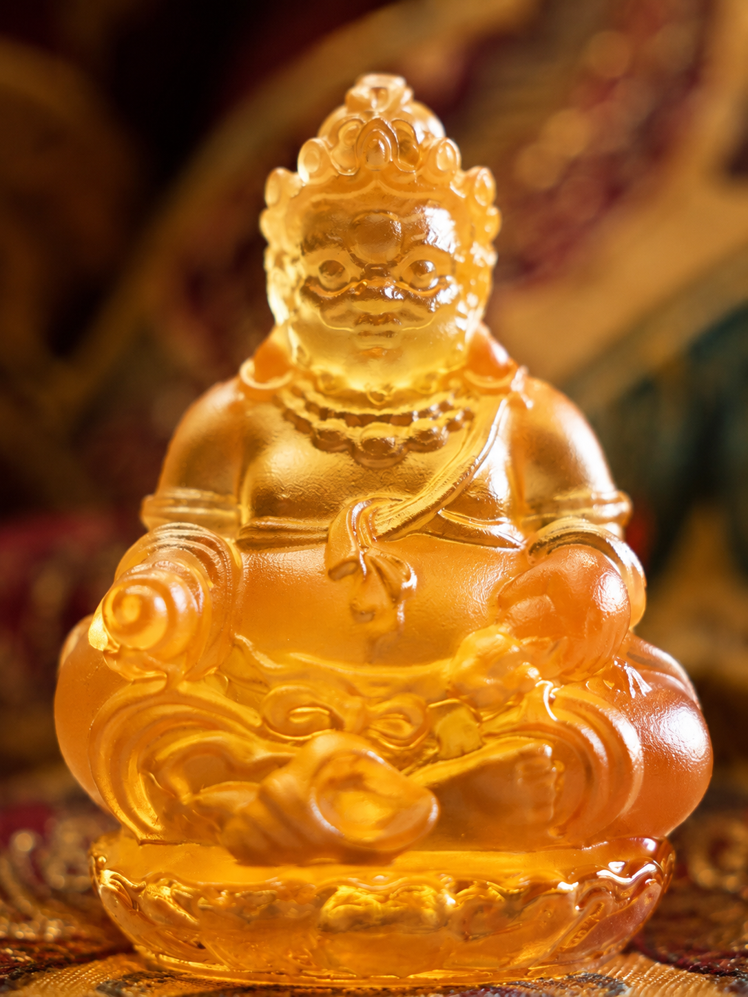 Close view of amber-colored liuli Yellow Jambhala, showing the face, jewelry, and seated figure
