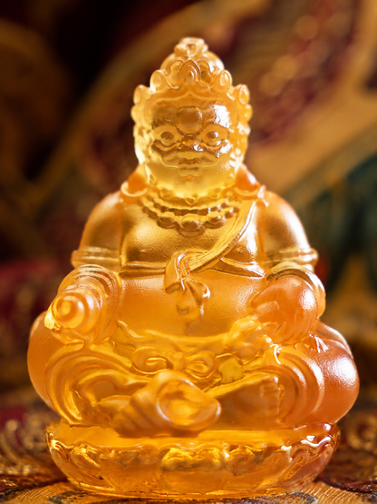 Close view of amber-colored liuli Yellow Jambhala, showing the face, jewelry, and seated figure