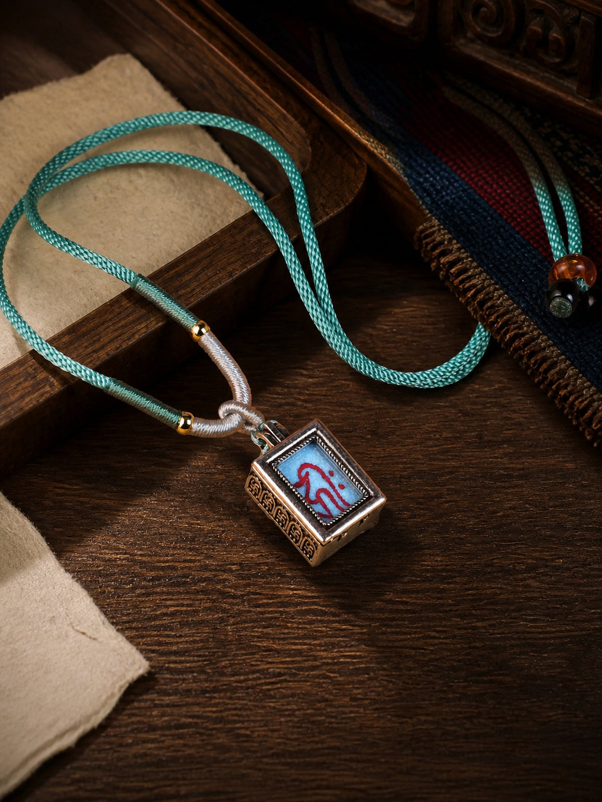 Thousand-Armed Avalokiteshvara design mini thangka pendant: painted symbol on pale blue, with a turquoise braided cord