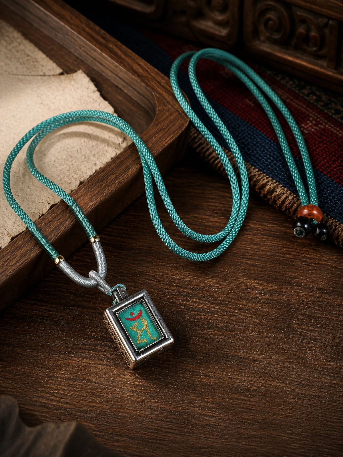 Manjushri Bodhisattva design mini thangka pendant: painted symbol on green, with a turquoise braided cord