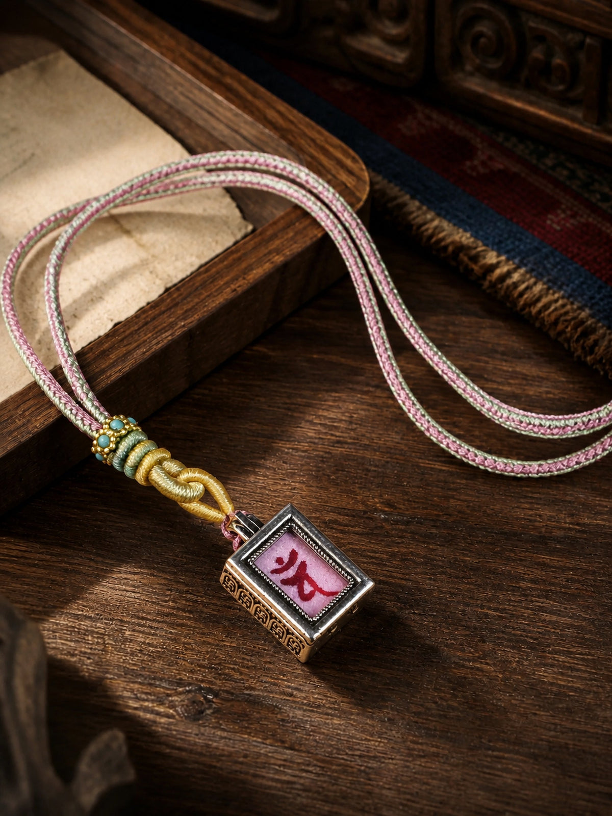 Vairocana Buddha design mini thangka pendant: painted symbol on pink, with a pink-and-cream braided cord