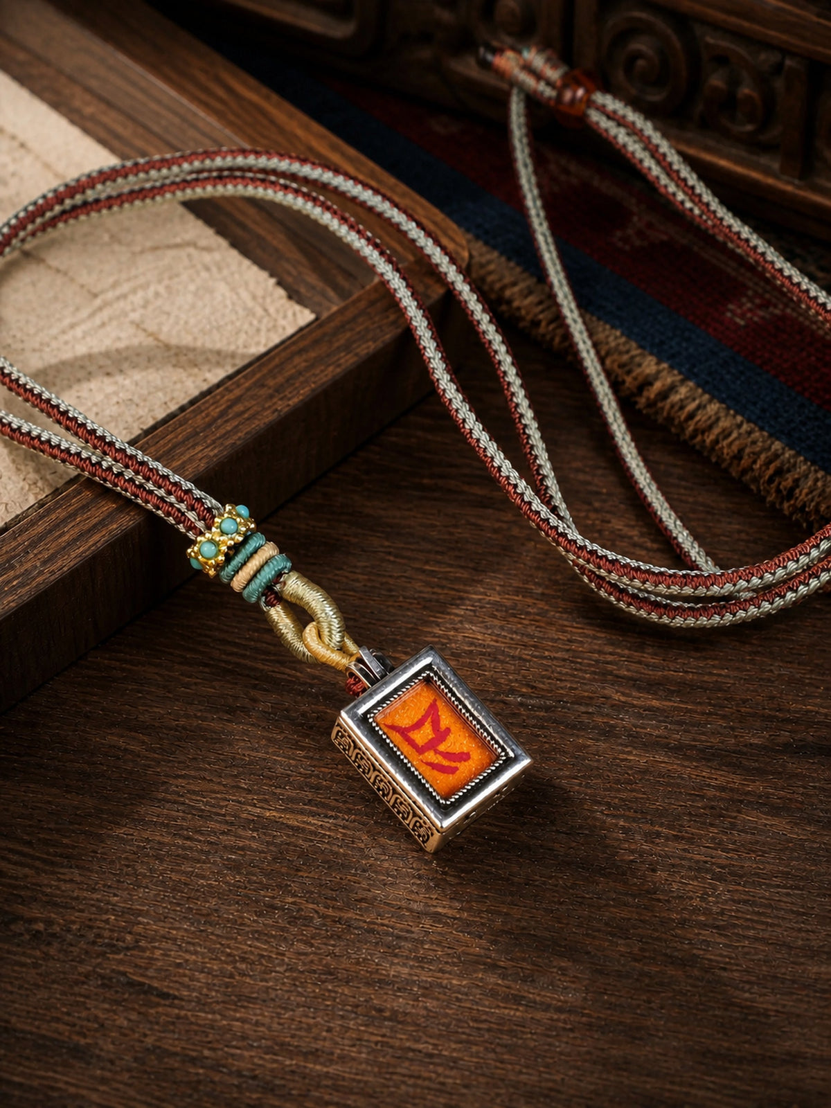 Vaishravana design mini thangka pendant: painted symbol on orange, with a red-and-gray braided cord