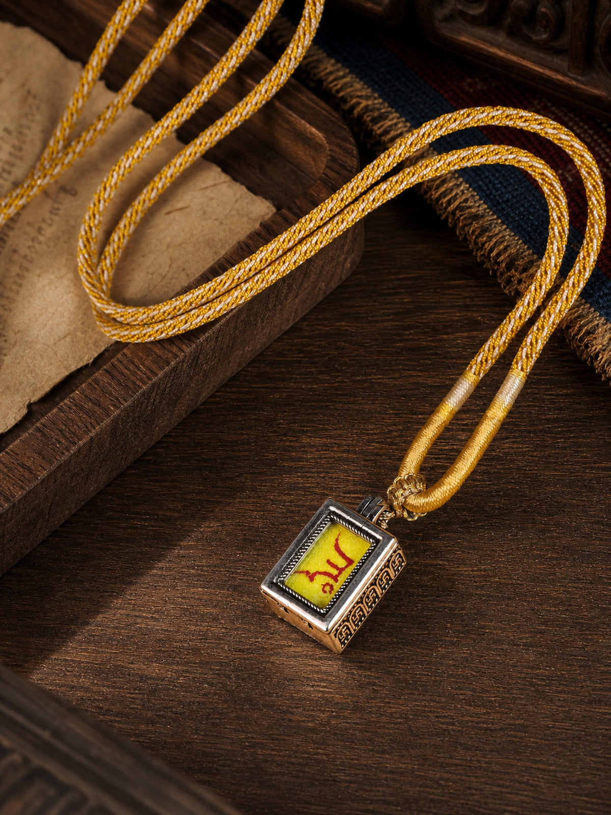 Yellow Jambhala design mini thangka pendant: painted symbol on yellow, with a golden braided cord