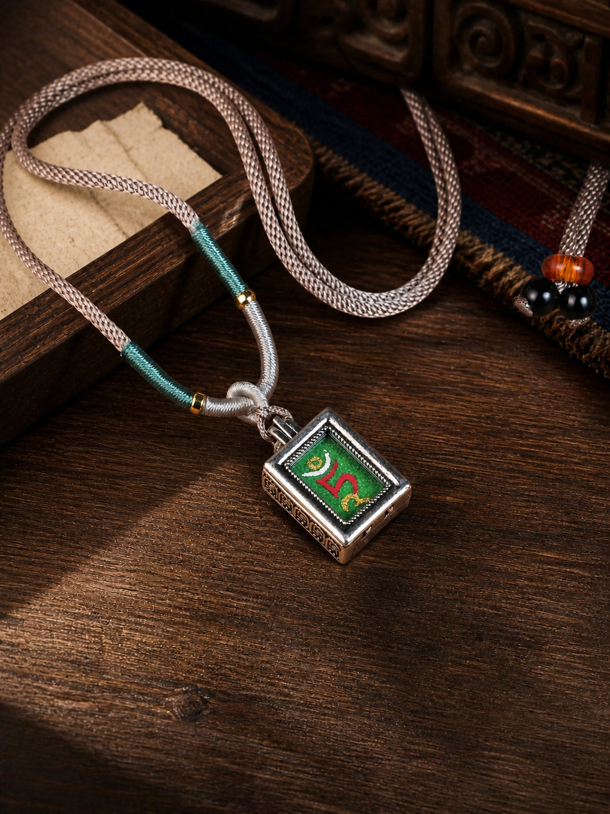 Green Tara design mini thangka pendant: painted symbol on green, with a pale pink braided cord