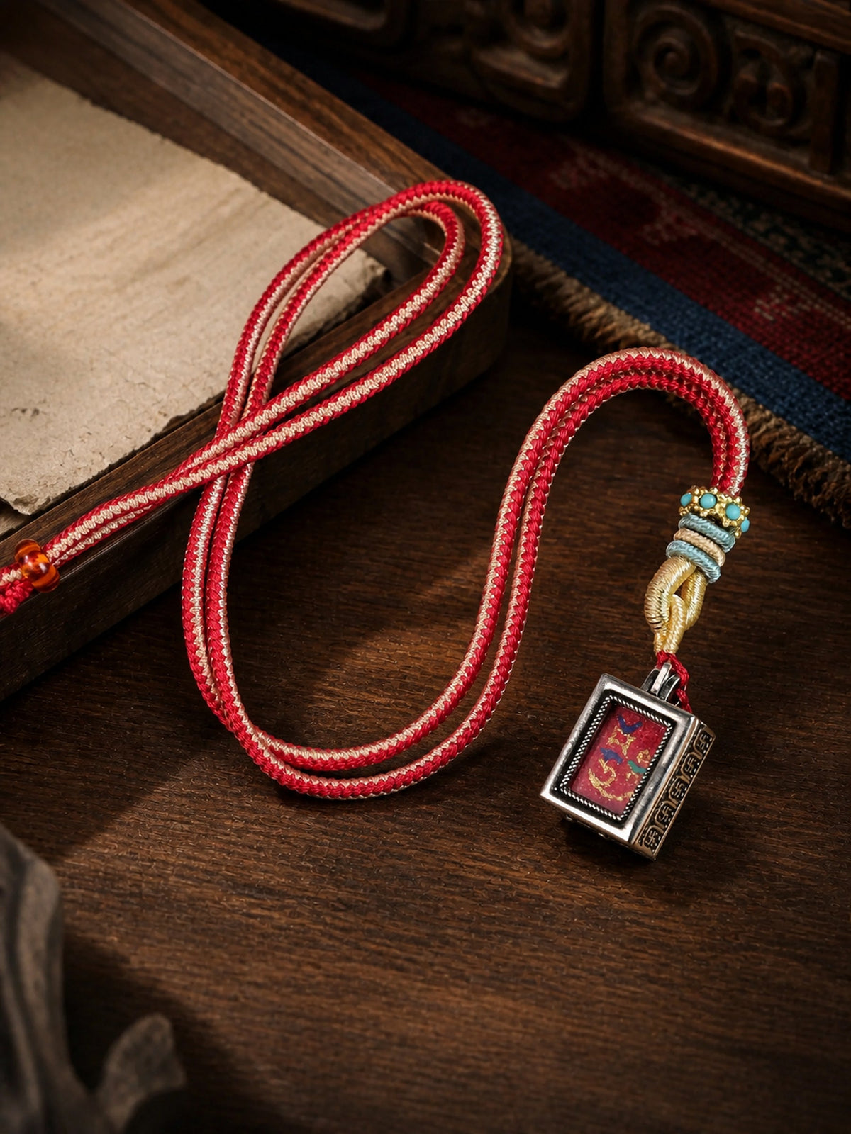 Zaki Lhamo — Style B design mini thangka pendant: painted symbol on red, with a red braided cord