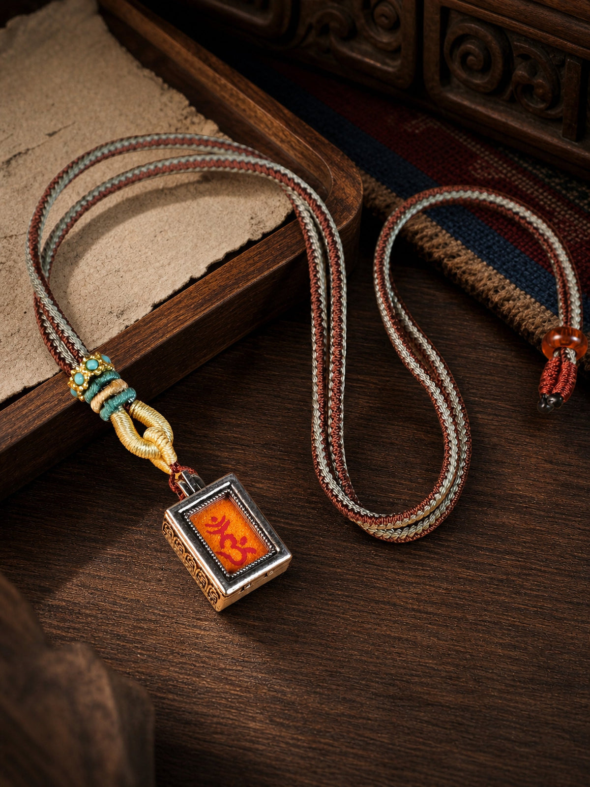 Shurangama Mantra design mini thangka pendant: painted symbol on orange, with a red-and-gray braided cord