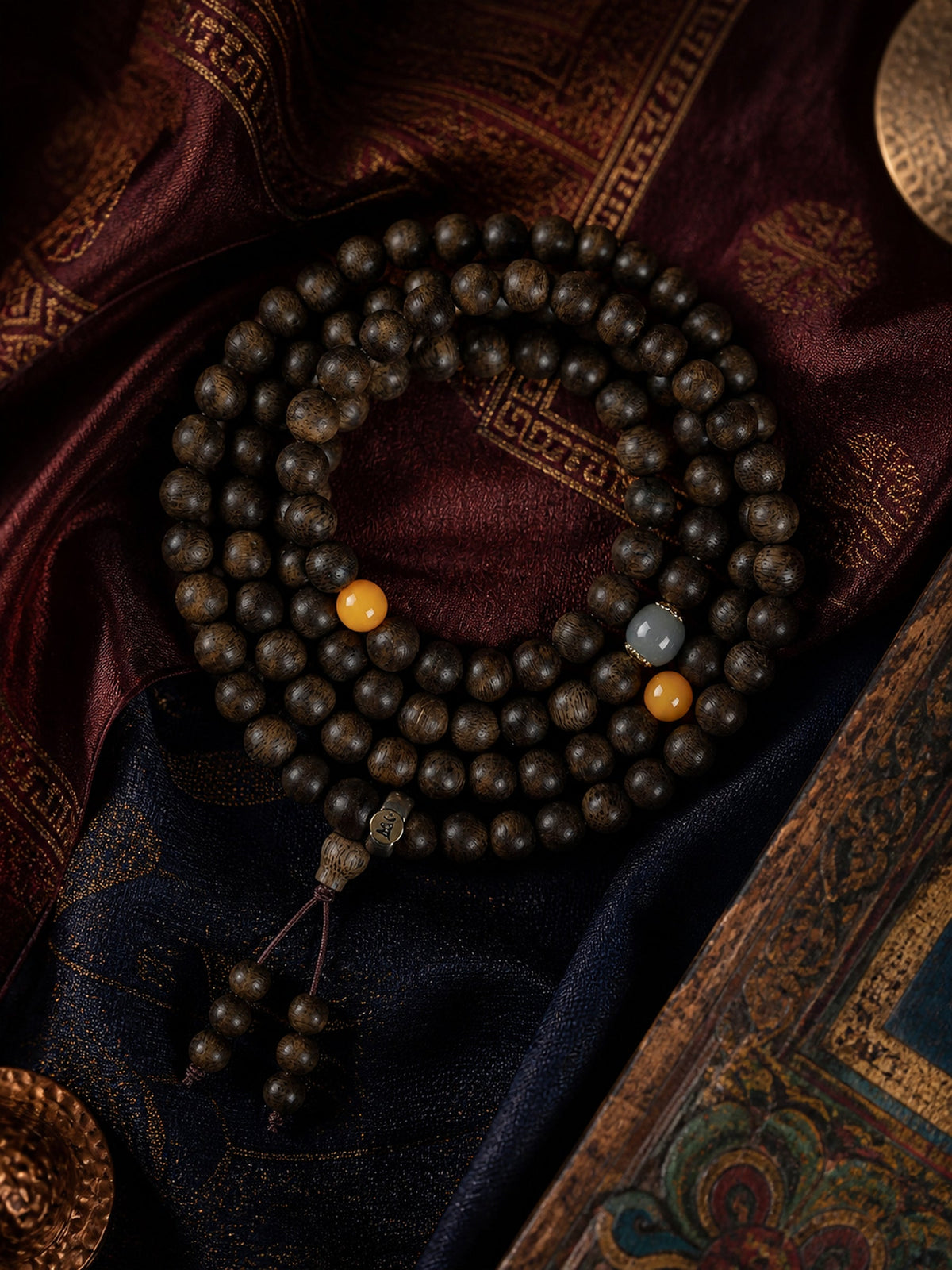 Full 108-bead agarwood mala bracelet arranged on rich woven textiles