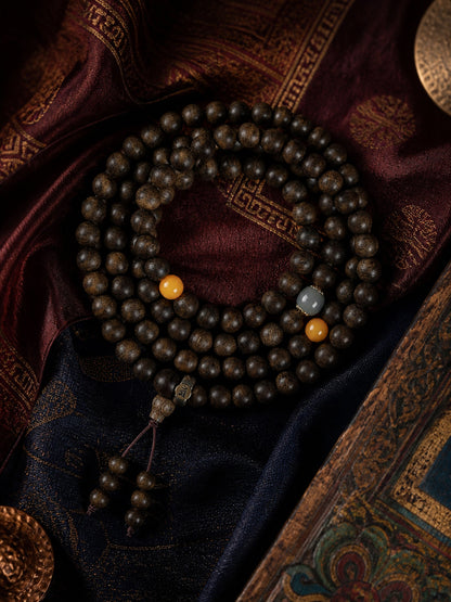 Full 108-bead agarwood mala bracelet arranged on rich woven textiles
