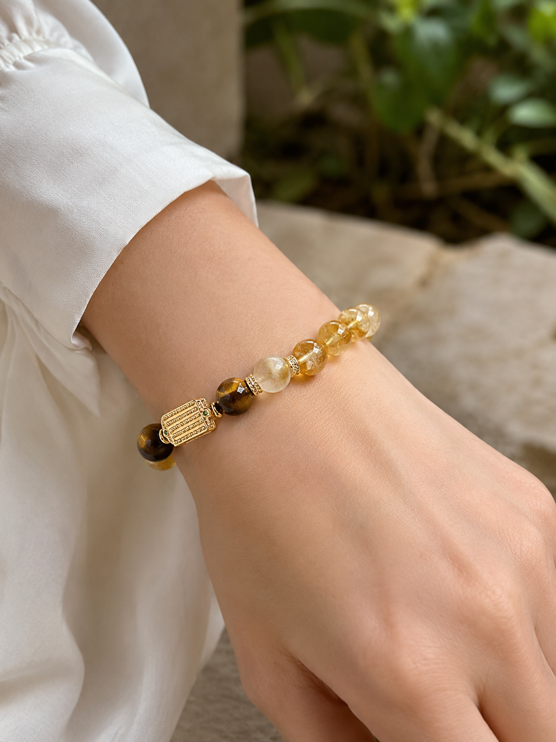 Yellow crystal and tiger's eye bracelet worn on the wrist beside a white cuff