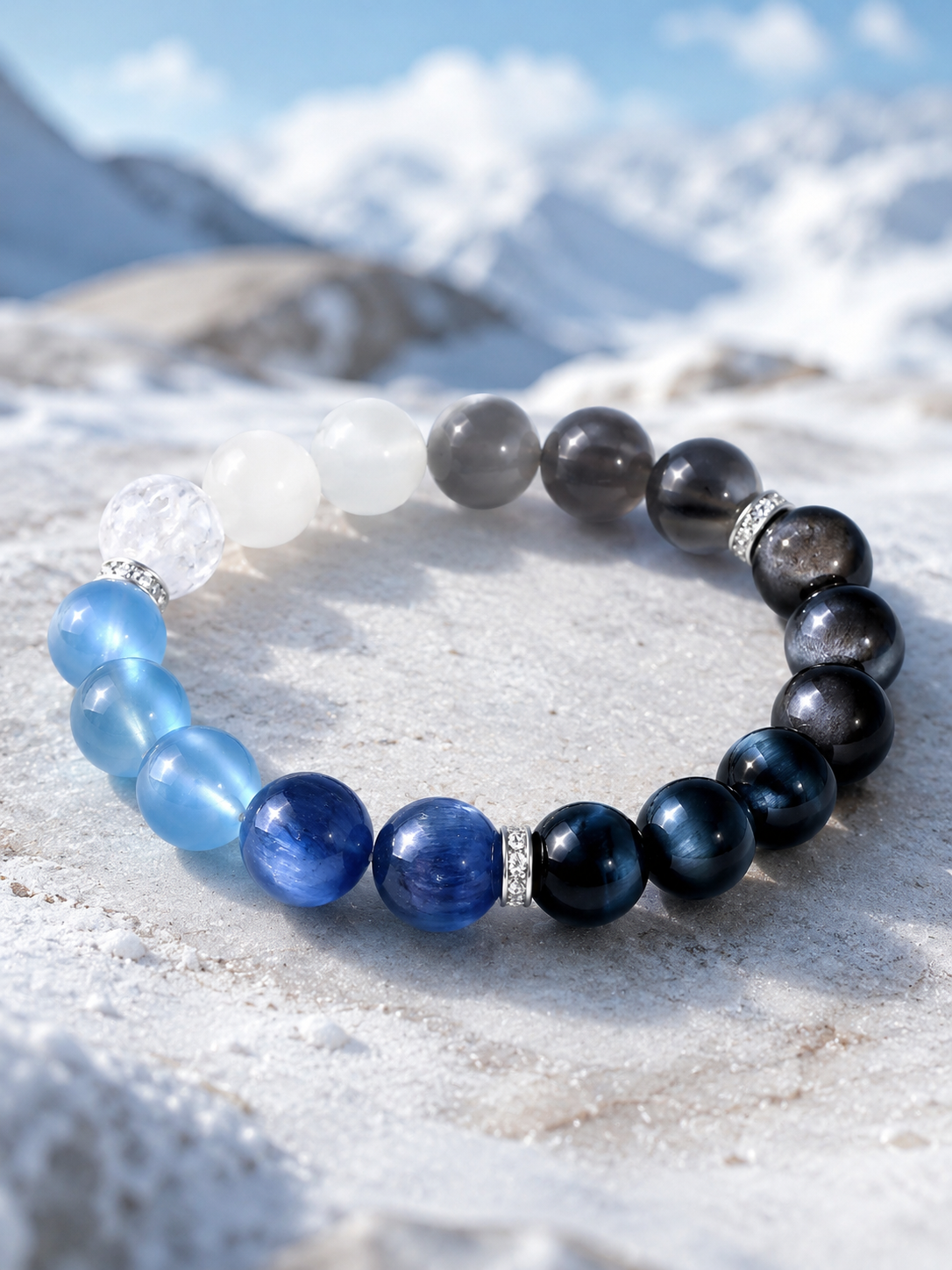 Five-Element blue crystal bracelet laid flat on pale rock with snowy mountains behind