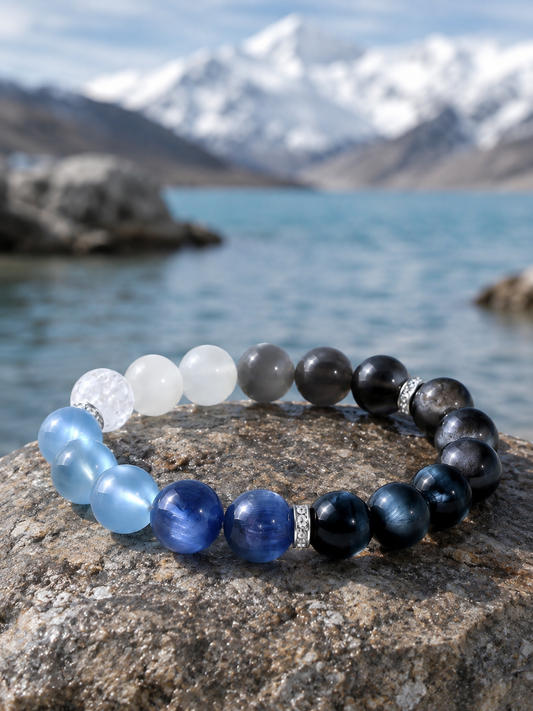 Five-Element blue crystal bracelet arranged on rock beside a lake, with beads grading from white to dark blue