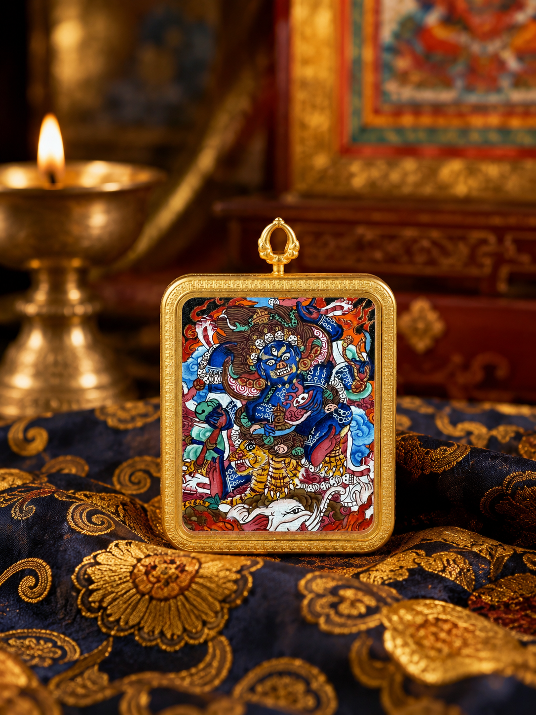 Mahakala thangka pendant in a gold-colored frame, standing on dark blue patterned fabric