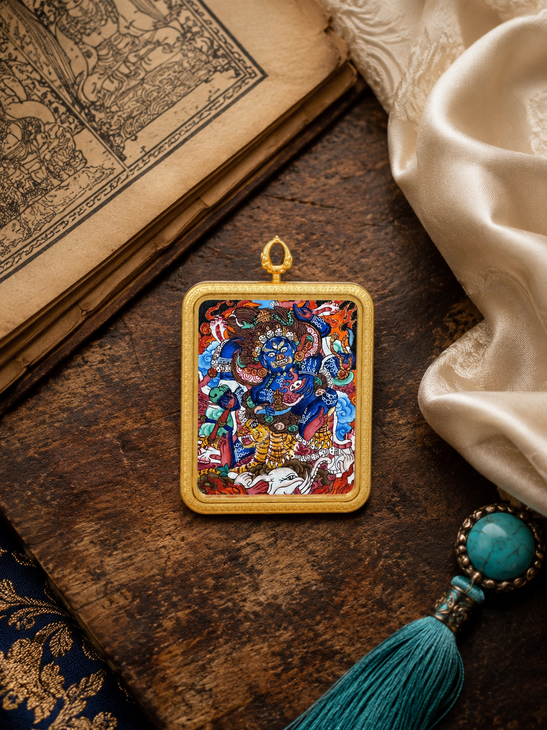 Mahakala thangka pendant lying beside printed pages and cream fabric
