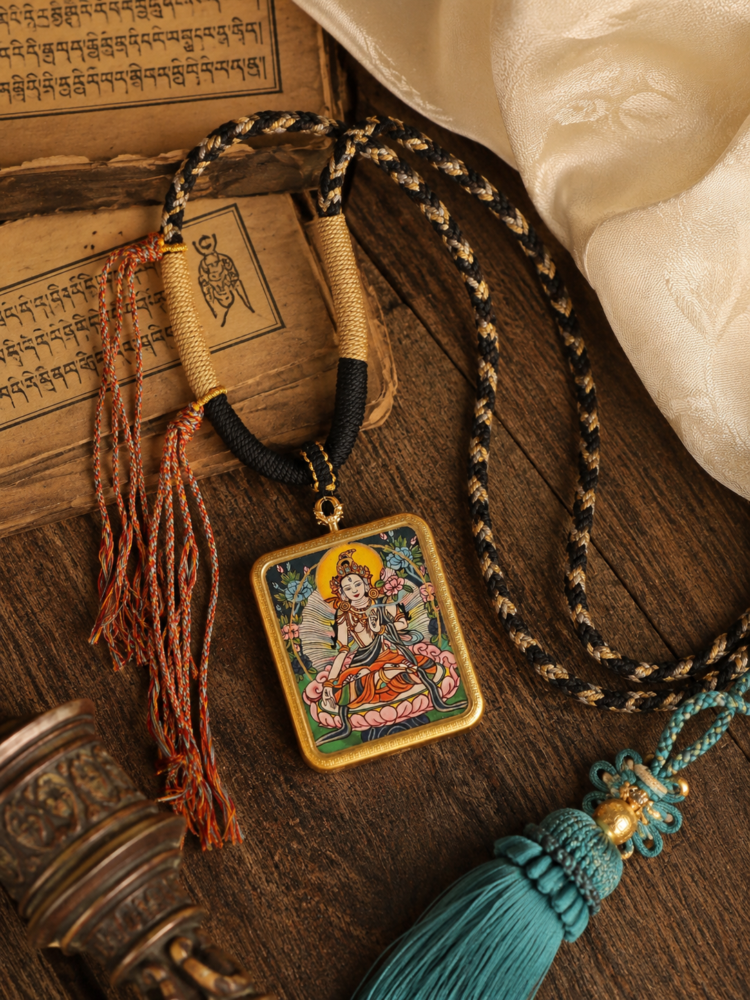 White Tara pendant and cord laid beside printed pages, with the long tassel visible