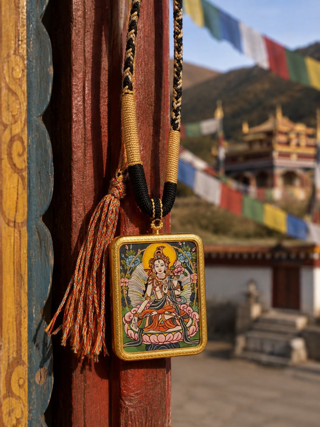 White Tara pendant hanging beside a painted wooden post with mountains in the background