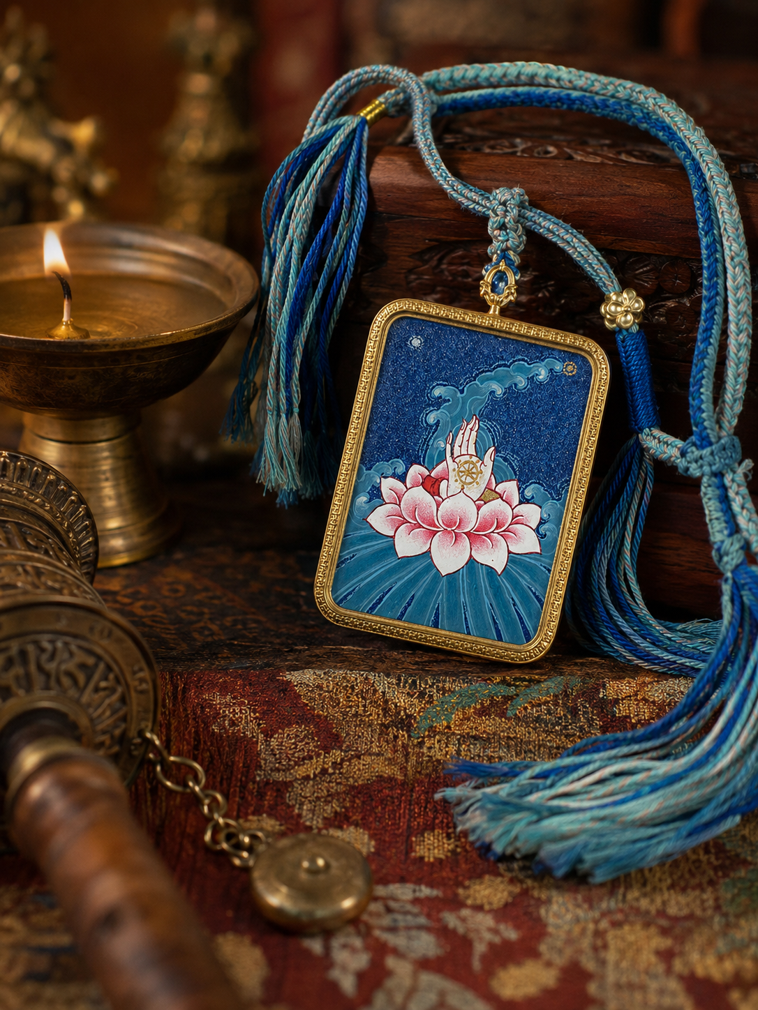 Lotus thangka pendant with a pink flower on blue, displayed with a blue tasseled cord