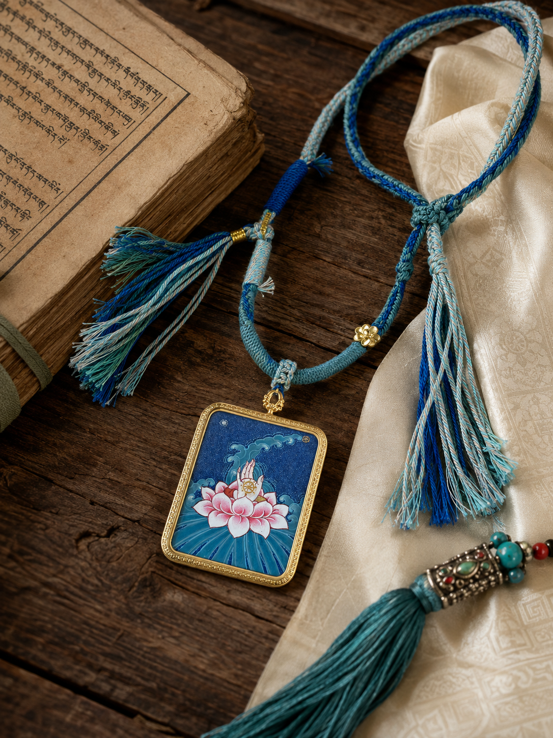 Lotus pendant and tasseled blue necklace laid beside cream fabric and printed pages