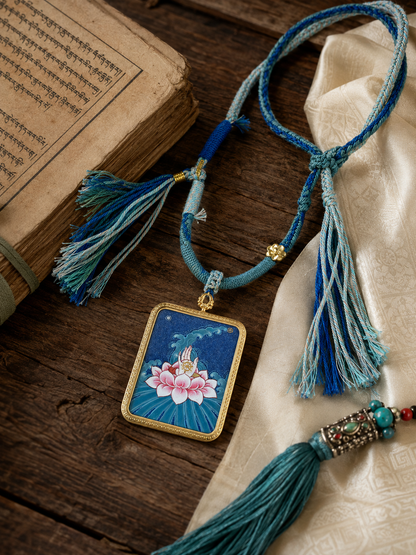 Lotus pendant and tasseled blue necklace laid beside cream fabric and printed pages