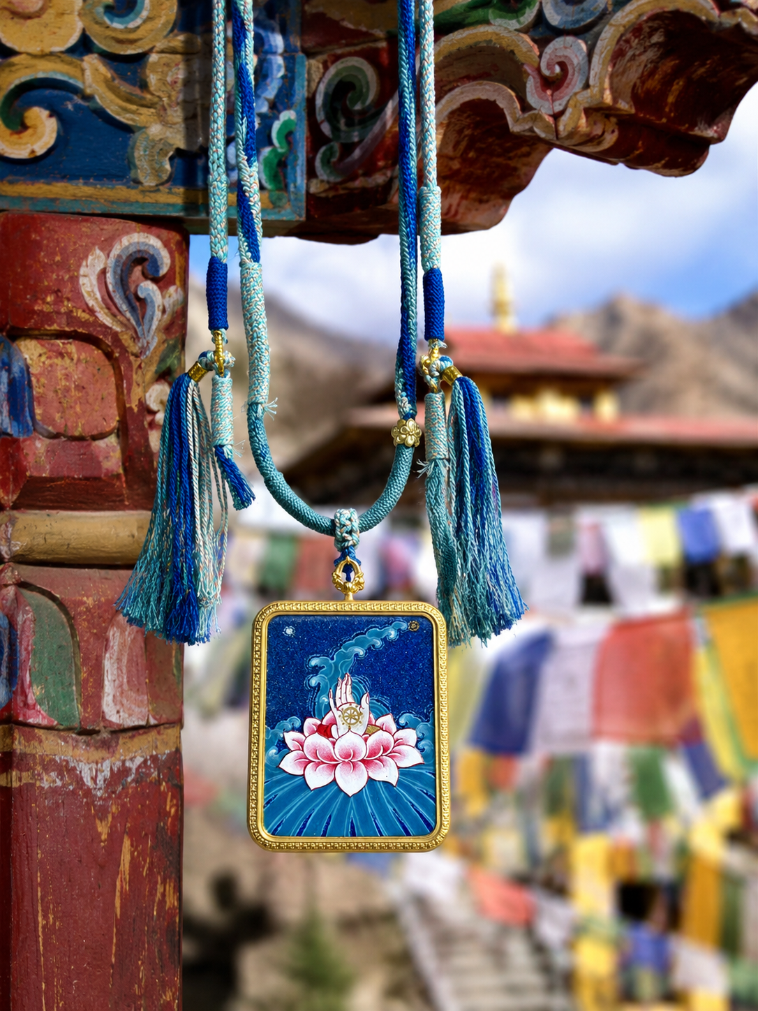 Pink lotus thangka pendant suspended from a blue cord beside a painted wooden beam