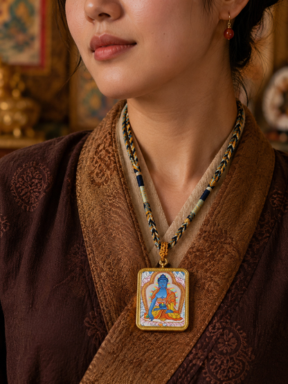 Medicine Buddha thangka pendant worn on a braided cord over brown clothing