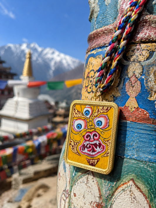 Yellow face-motif pendant hanging from a braided cord beside a brightly painted post