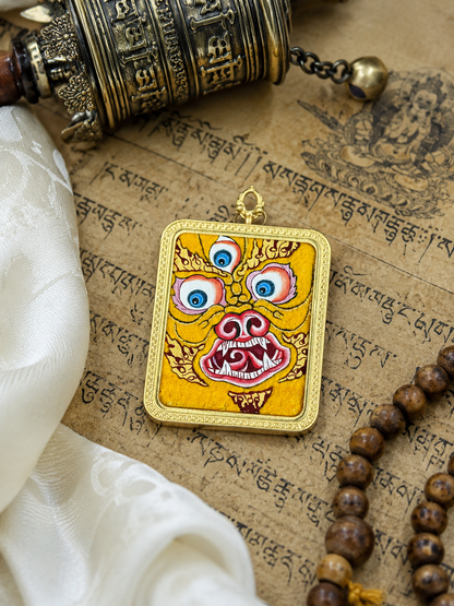 Close view of the three-eyed face motif on the yellow pendant, laid on printed pages