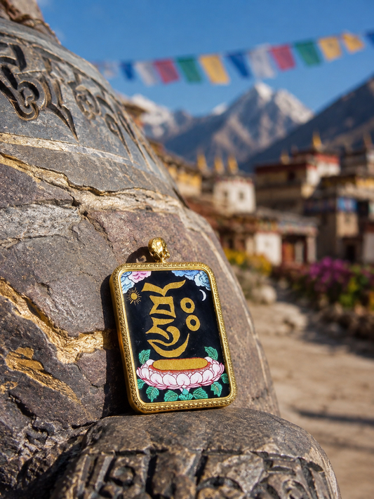Zaki Lhamo Heart Mantra pendant resting against a stone, with mountains and prayer flags behind