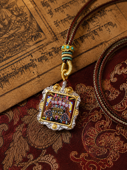 Square Zaki Lhamo ghau pendant laid on patterned fabric beside printed pages